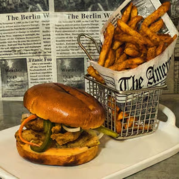 A burger with pickles and onions next to a metal basket of fries, served on a white tray.