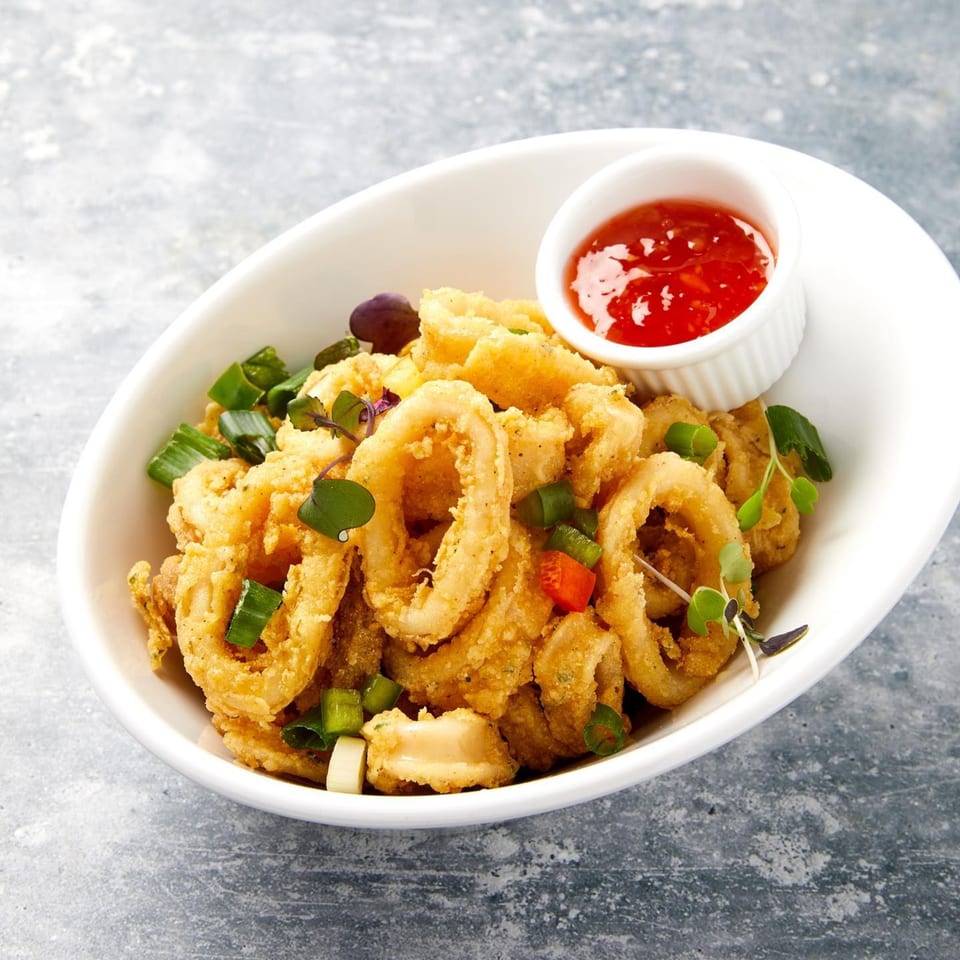 Crispy fried calamari rings with green onions, microgreens, and a side of sweet chili sauce.