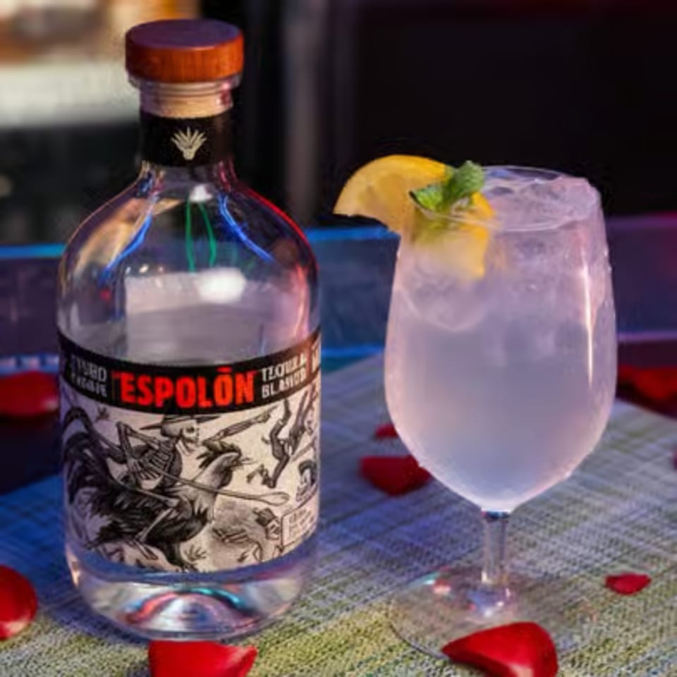 A bottle of Espolòn Tequila Blanco next to a cocktail garnished with lemon and mint.