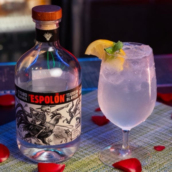 A bottle of Espolòn Tequila Blanco next to a cocktail garnished with lemon and mint.