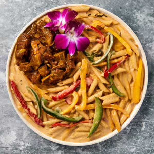 Oxtail and pasta with bell peppers in a creamy sauce, garnished with purple orchids.
