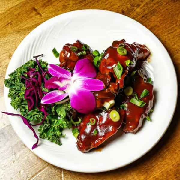 Sweet and sour chicken wings garnished with green onions, kale, red cabbage, and a purple orchid.