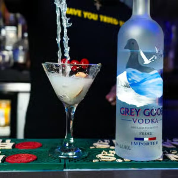 A Grey Goose vodka bottle next to a martini glass with cherries, being poured a drink.