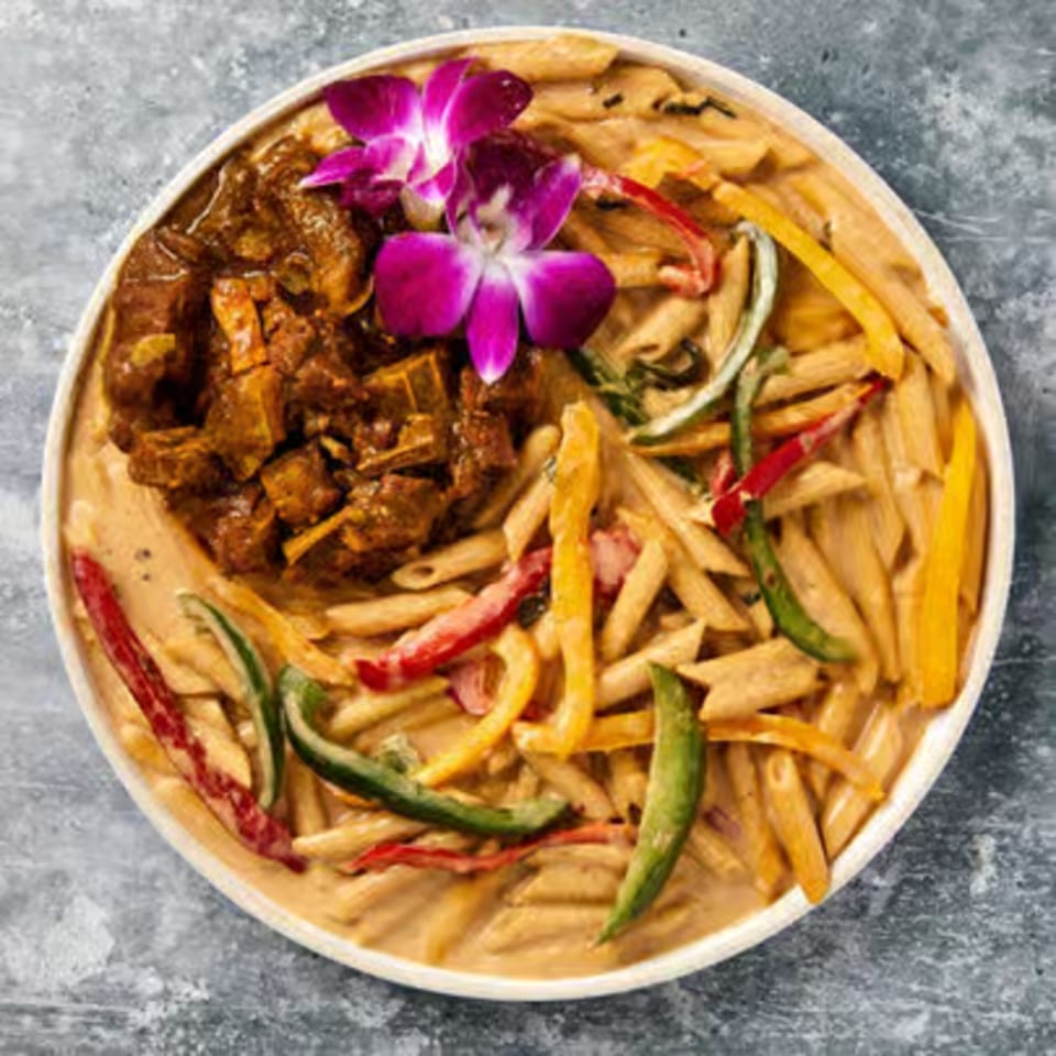 Oxtail and penne pasta with bell peppers and purple orchids in a white bowl.
