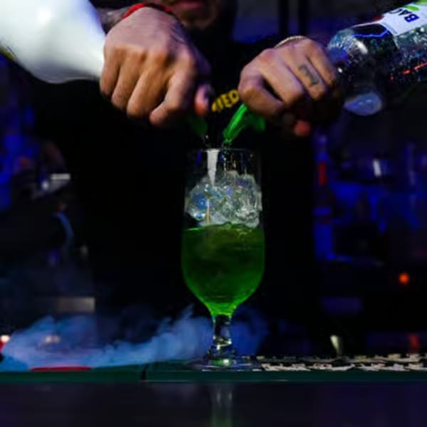 Bartender pouring a green cocktail into a glass with ice, creating a splash.