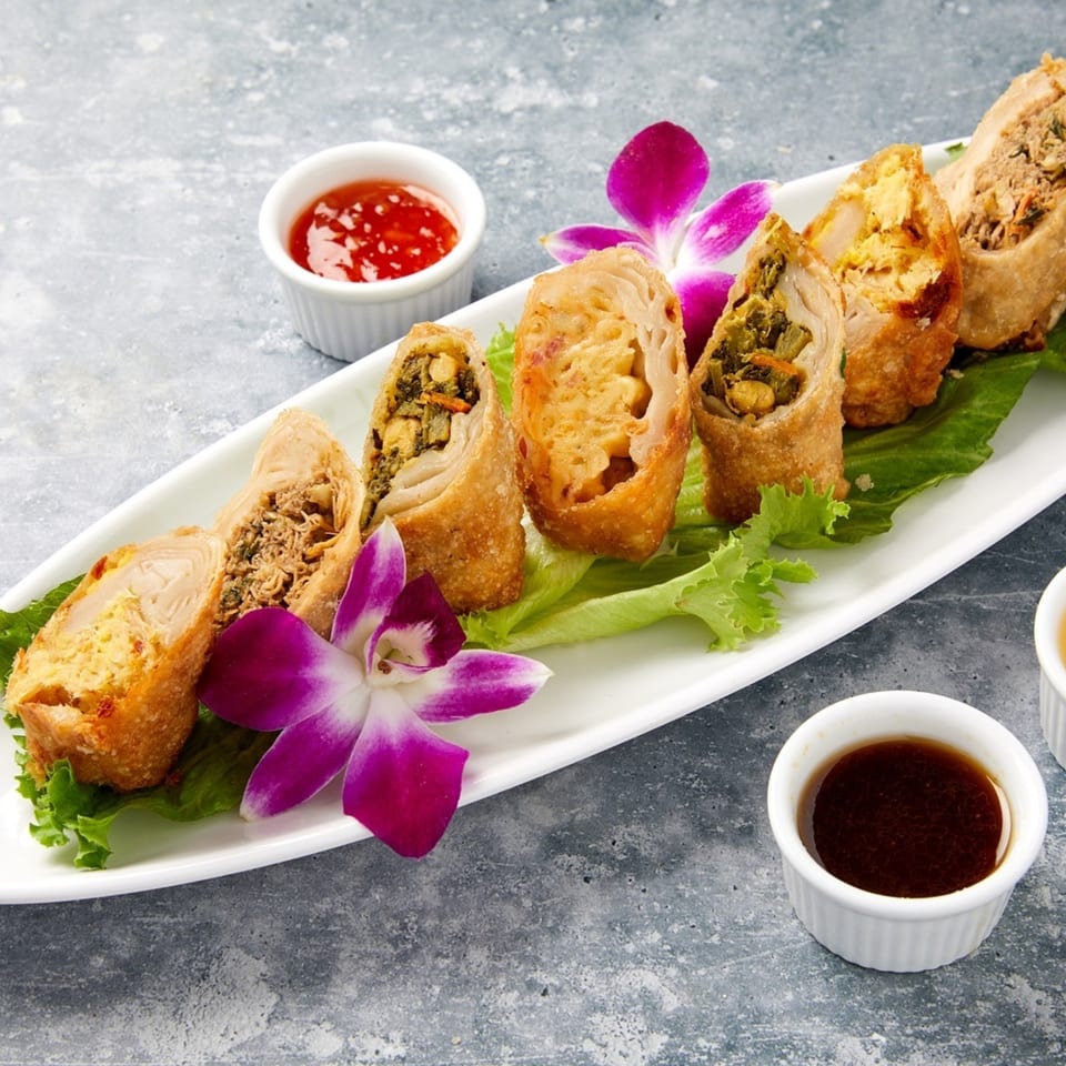 Crispy spring rolls with various fillings, garnished with lettuce and purple orchids, served with dipping sauces.